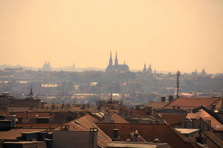 Hitzekuppel über Europa — dunstiges, glühendes Sommerhimmel über den Dächern einer mitteleuropäischen Stadt während der Hitzewelle