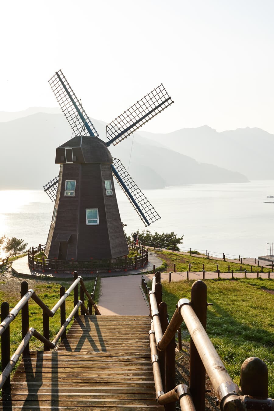 A traditional wooden windmill on a hill overlooking a lake with mountains in the background during s
