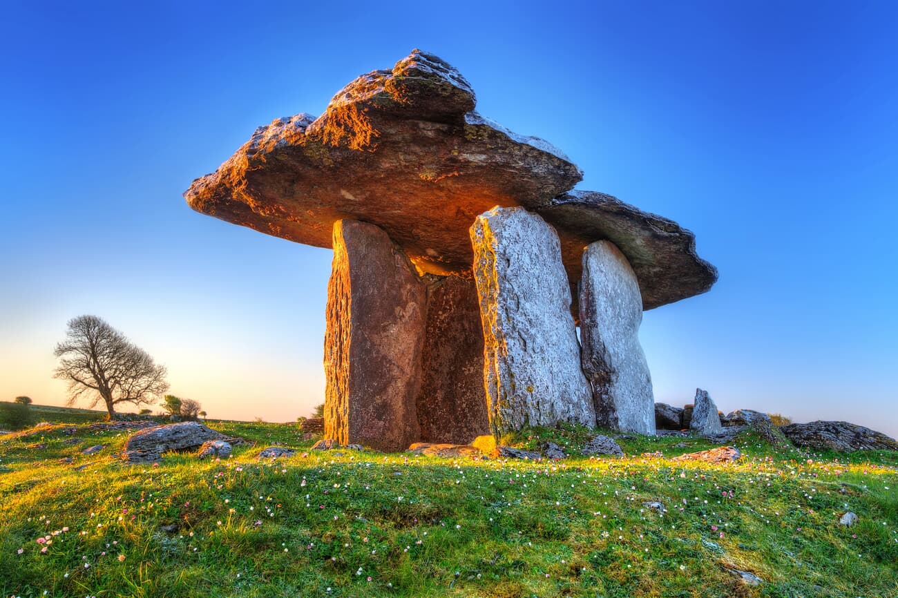 A Neolithic dolmen with a large capstone resting on three upright stones against a clear blue sky du