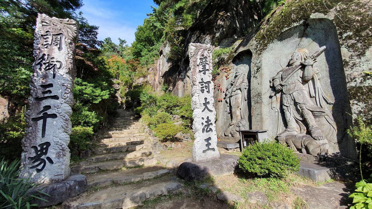 Stone carvings and pillars with engraved text at a serene Japanese temple grounds, surrounded by lus