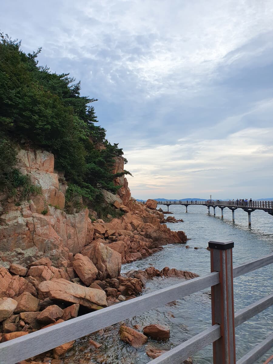 A scenic coastal view with a rocky shoreline and a wooden pier extending into the water, surrounded 
