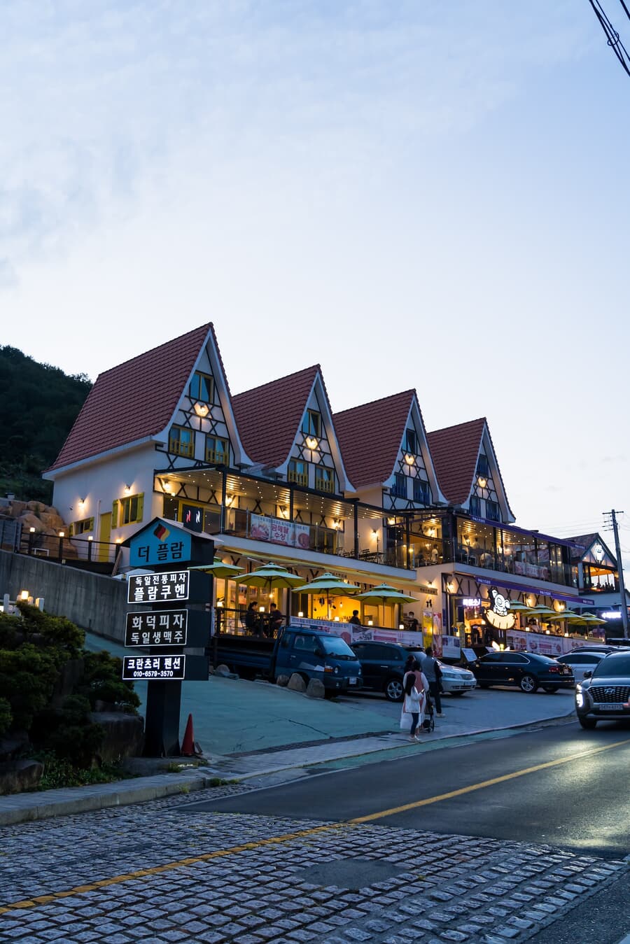 A two-story building with a pitched roof featuring dormer windows illuminated at twilight, with seve