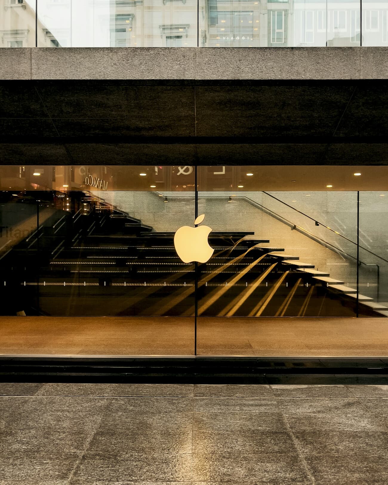 The glass entrance and interior staircase of Appleโs Piazza Liberty store in Milan, viewed at street level