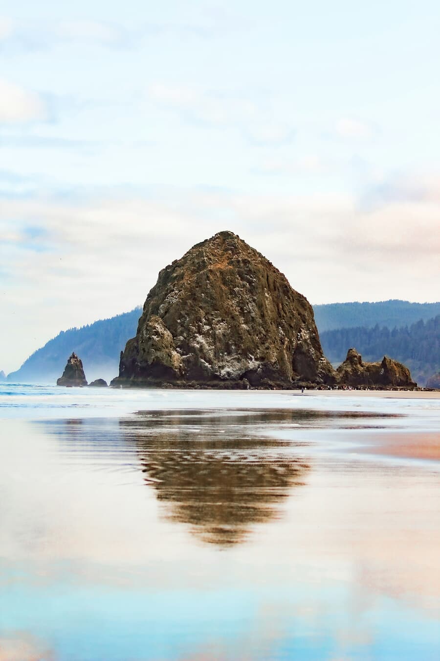 Haystack Rock reflects on the wet sand at low tide in Cannon Beach, Oregon