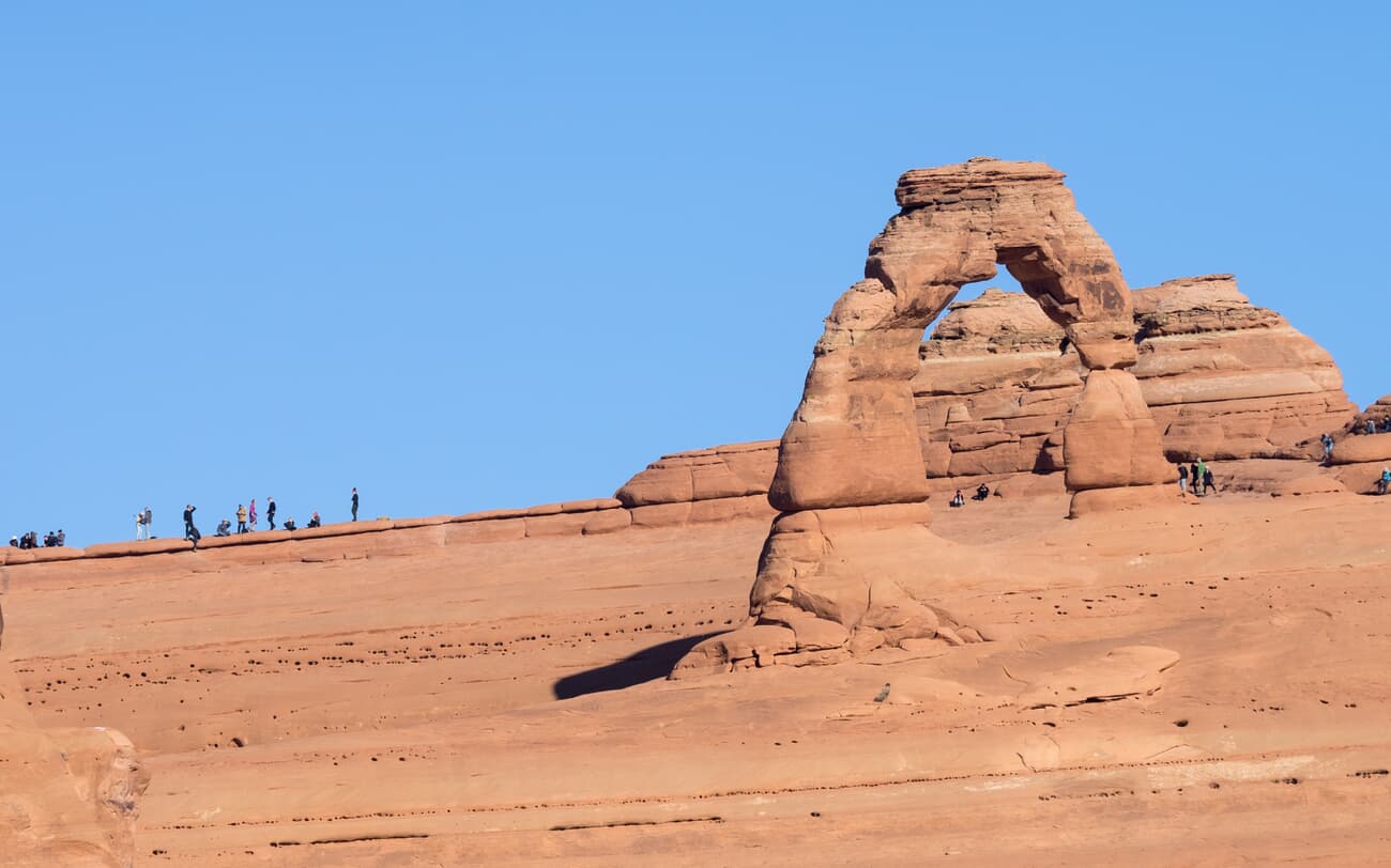Hikers gather beneath Delicate Arch, the sandstone icon of Arches National Park near Moab, Utah