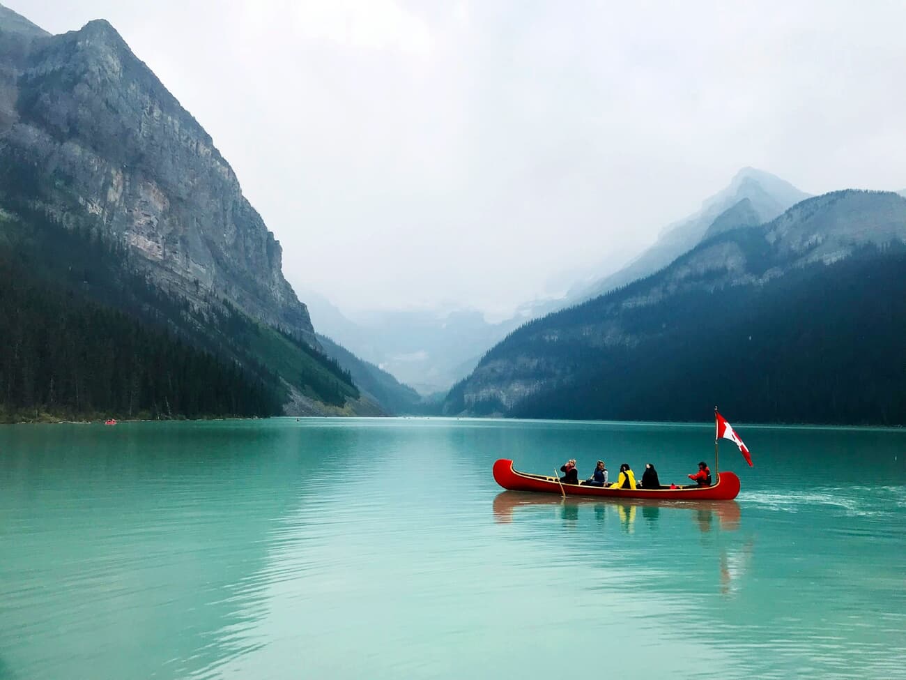 A red canoe crosses the glacial turquoise water of Lake Louise in Banff National Park, Canada