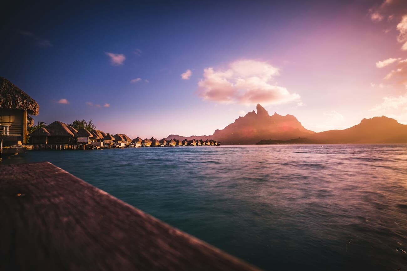 Overwater bungalows line the lagoon beneath Mount Otemanu at sunset in Bora Bora, French Polynesia