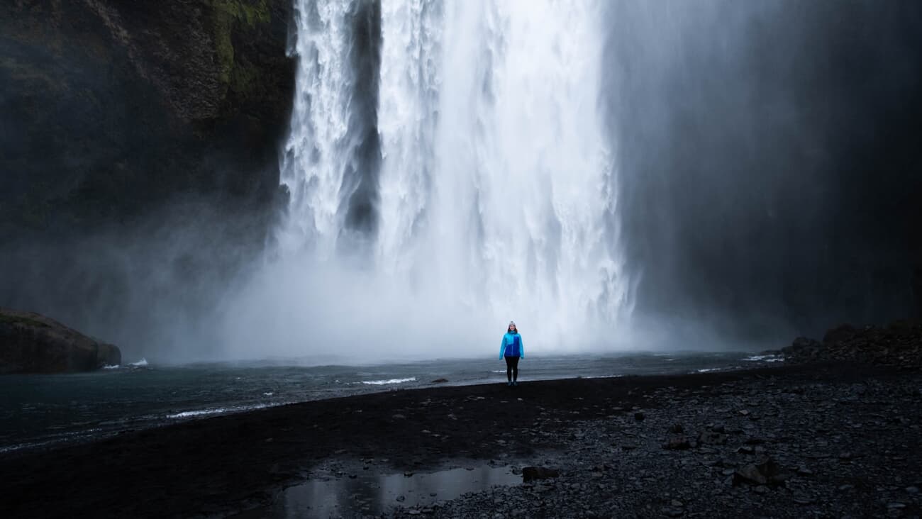 A lone figure stands beneath the full force of Skógafoss waterfall in southern Iceland