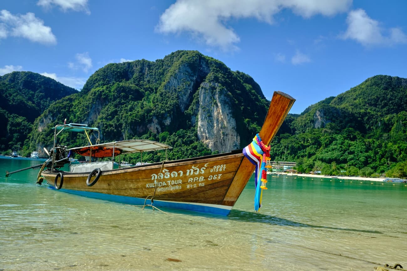 A longtail boat floats on clear water beneath the limestone cliffs of Thailand's Andaman coast