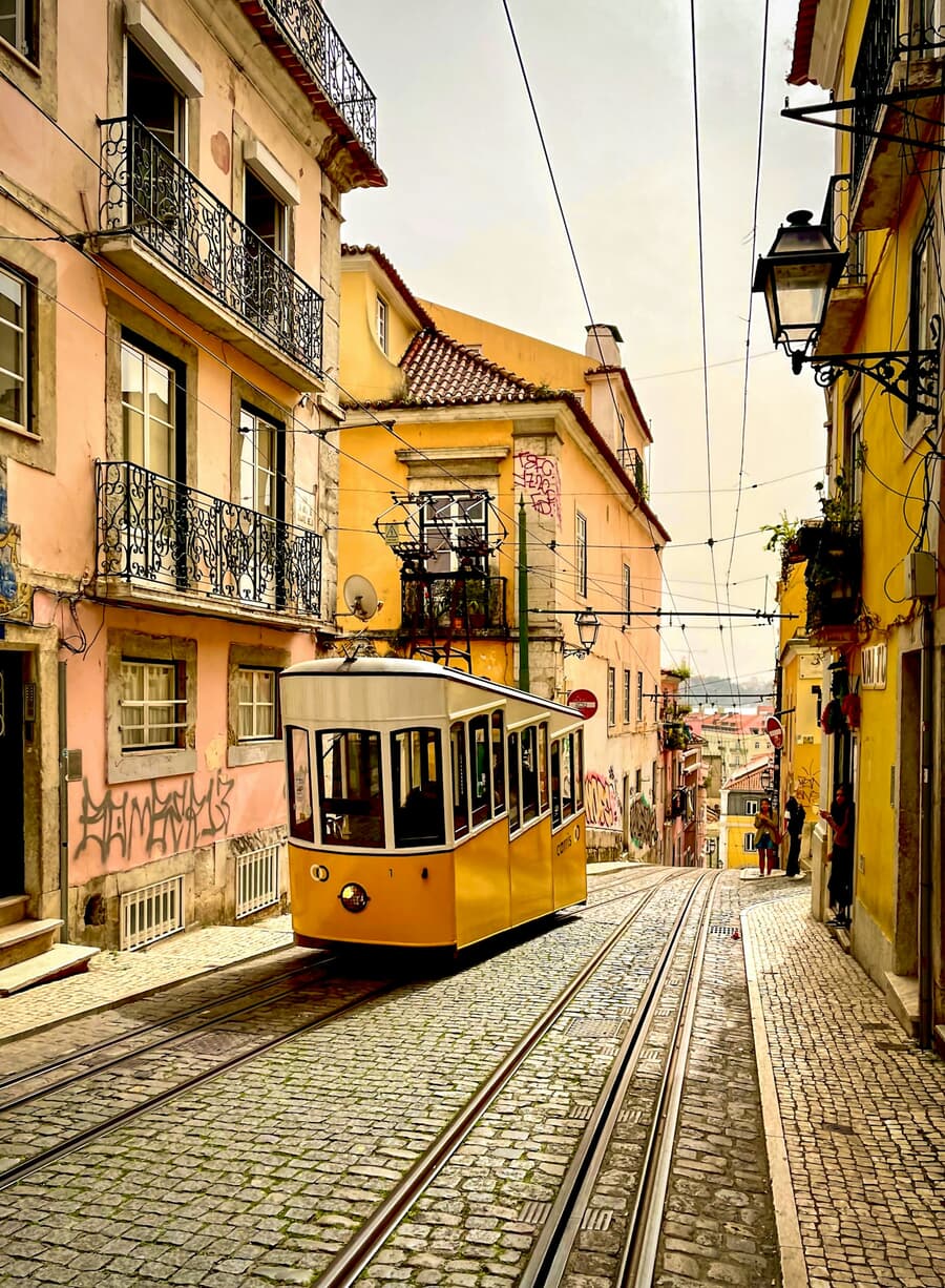 A yellow tram climbs a narrow tiled street in Lisbon, Portugal