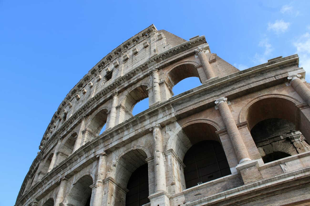 The Colosseum's arched tiers rise against a blue sky in the heart of Rome, Italy