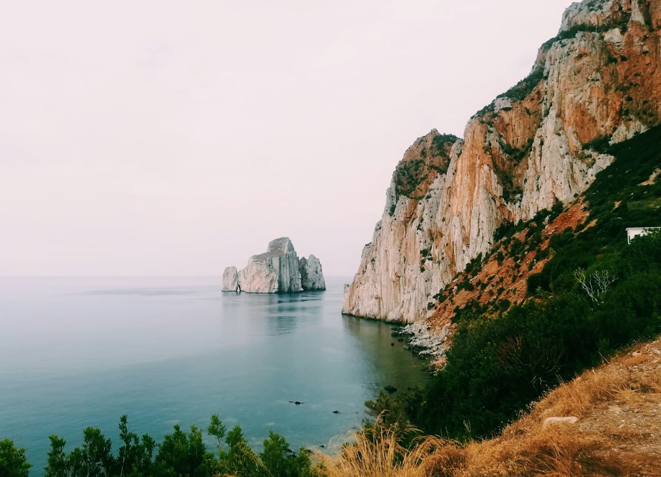 White limestone cliffs and a sea stack meet clear water on Sardinia's Masua coast, Italy
