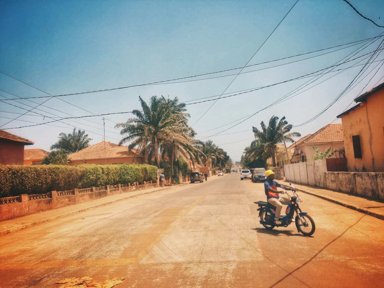 A sunlit red-dirt street with palms and a motorbike in Bissau, Guinea-Bissau