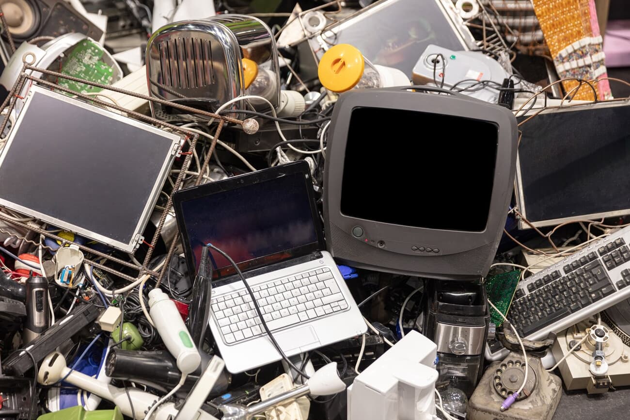 Pile of discarded electronic waste including a laptop, CRT television, keyboards, LCD screens, a toaster and tangled cables