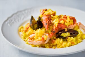 A plate of seafood paella with shrimp and mussels on a light background.