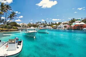 A scenic view of a harbor in Bermuda with clear turquoise waters, boats, and colorful buildings along the shore.