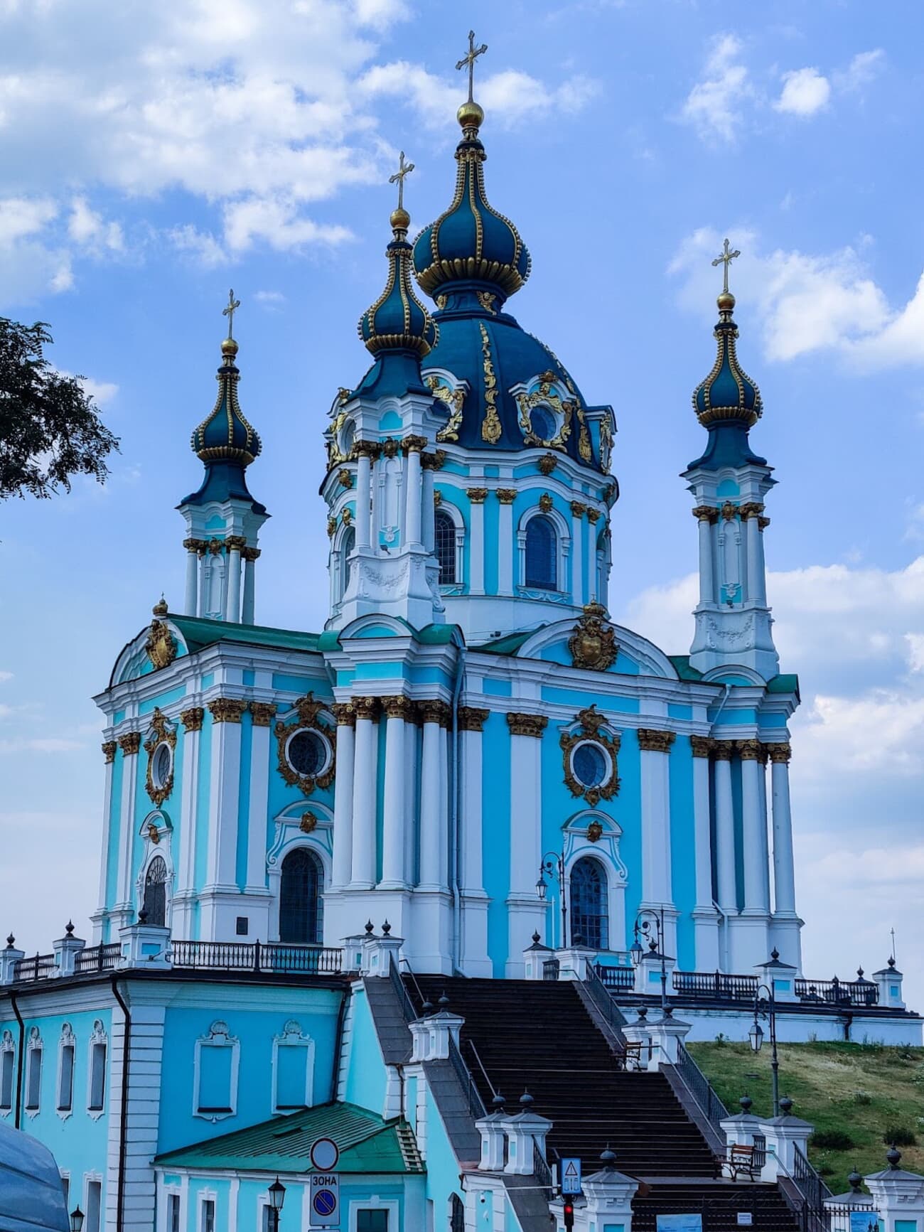 A photo shows St. Andrew's Church's blue facade, white details, gold accents, and dark domes with golden crosses.
