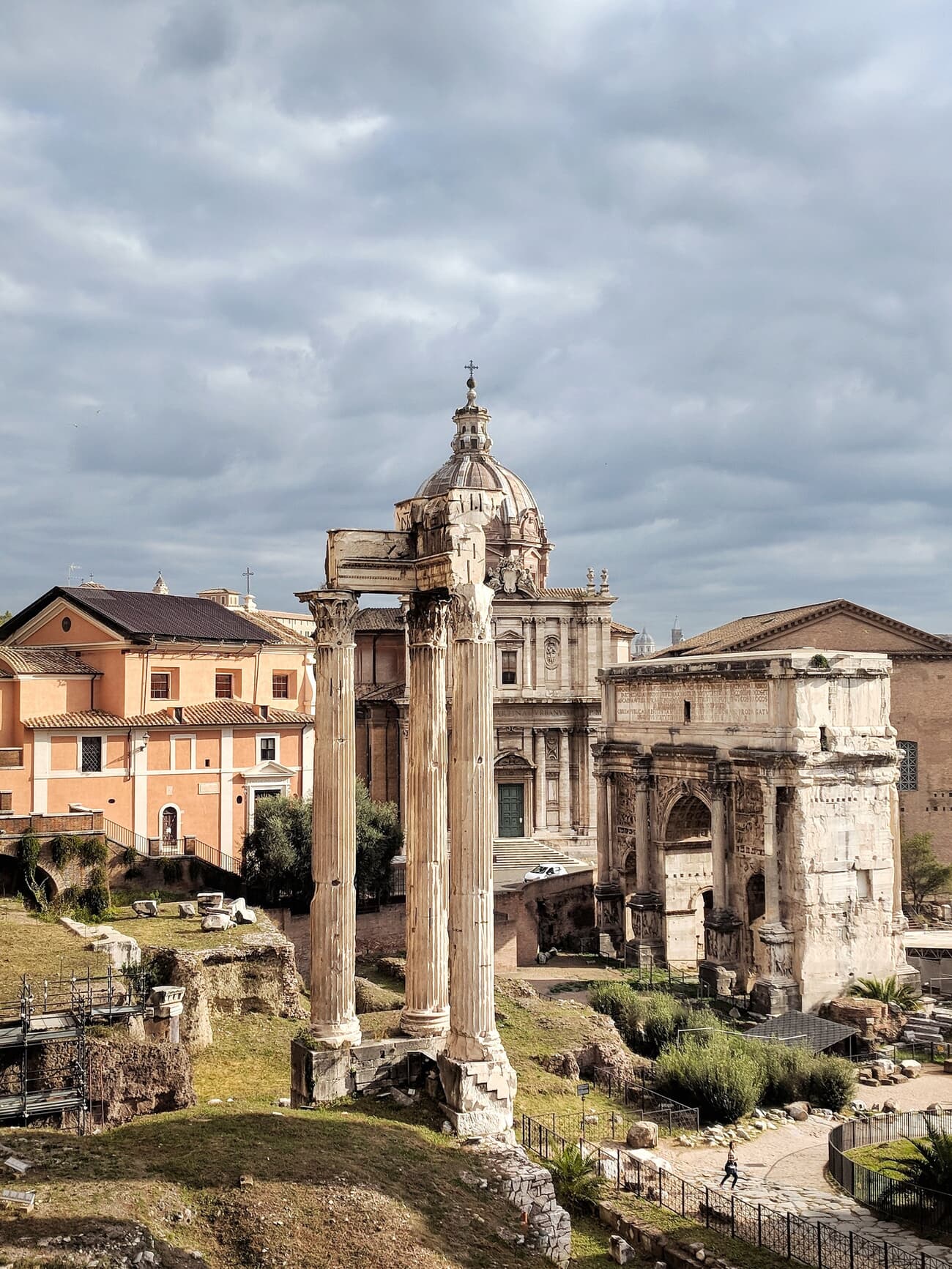 An image of the Arch of Severus at the Roman Forum, featuring ancient Roman ruins with columns and arches under a cloudy sky.