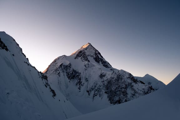 The snowy summit of the Gasherbrum mountain stands in a clear, dusk sky.