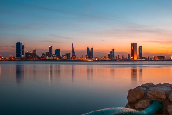 The city skyline of Manama in Bahrain is illuminated across the water at dusk.