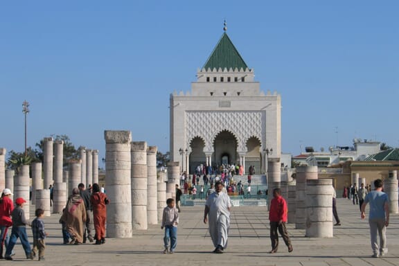 A crowd of people walk around the entrance to the Mausoleum of Mohammed V.