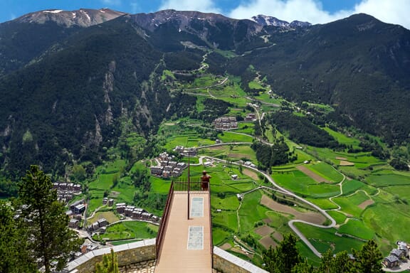 Green fields between mountains can be seen beneath the Mirador Roc del Quer observation deck in Andorra.