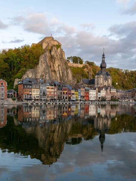 Buildings sit next to the water and in front of a rock face in Dinant, Belgium. Buildings sit next to the water and in front of a rock face in Dinant, Belgium.