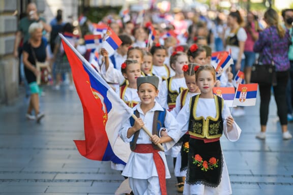 Young children dressed up in traditional handmade folk costumes outfit from the Republic of Serbia holding Serbia flags, walking trough national street festival parade. 15.09.2021 Belgrade, Serbia
