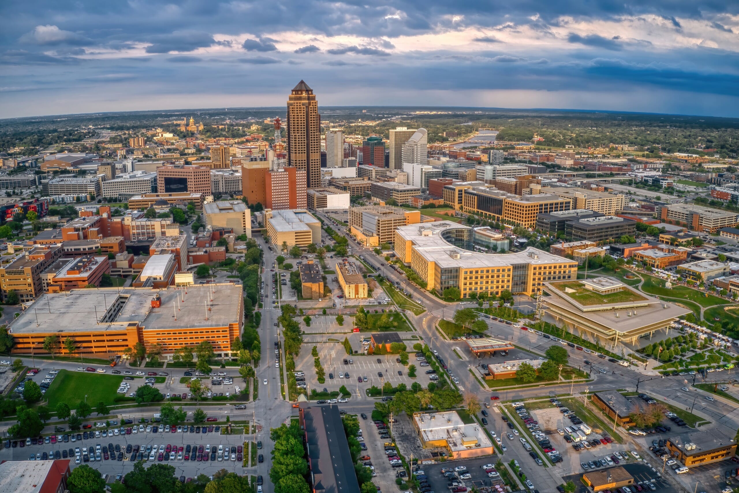 Aerial view of a cityscape at dusk, featuring a mix of high-rise and low-rise buildings, with the tallest skyscraper near the center surrounded by various commercial buildings, streets, parking lots, <a href=
