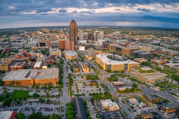 Aerial view of a cityscape at dusk, featuring a mix of high-rise and low-rise buildings, with the tallest skyscraper near the center surrounded by various commercial buildings, streets, parking lots, <a href=