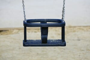 An empty blue baby swing hanging from chains, symbolizing falling birth rates and global population decline